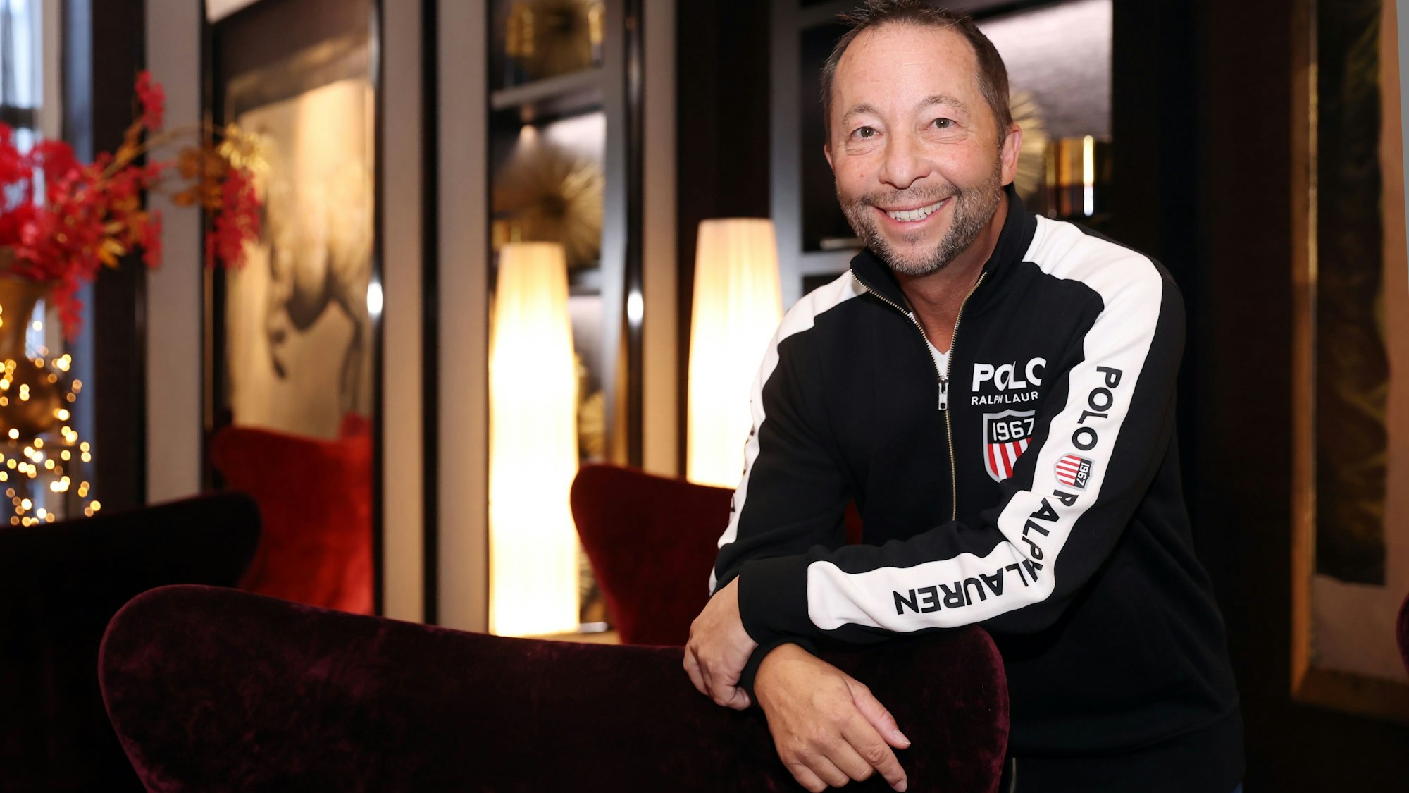 DJ Bobo in einer Sweatjacke lehnt an einem roten Sessel.
