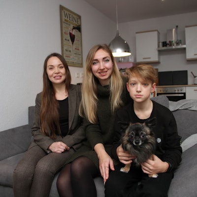 Die drei sitzen mit dem Chihuahua auf einem Sofa in ihrer Küche.