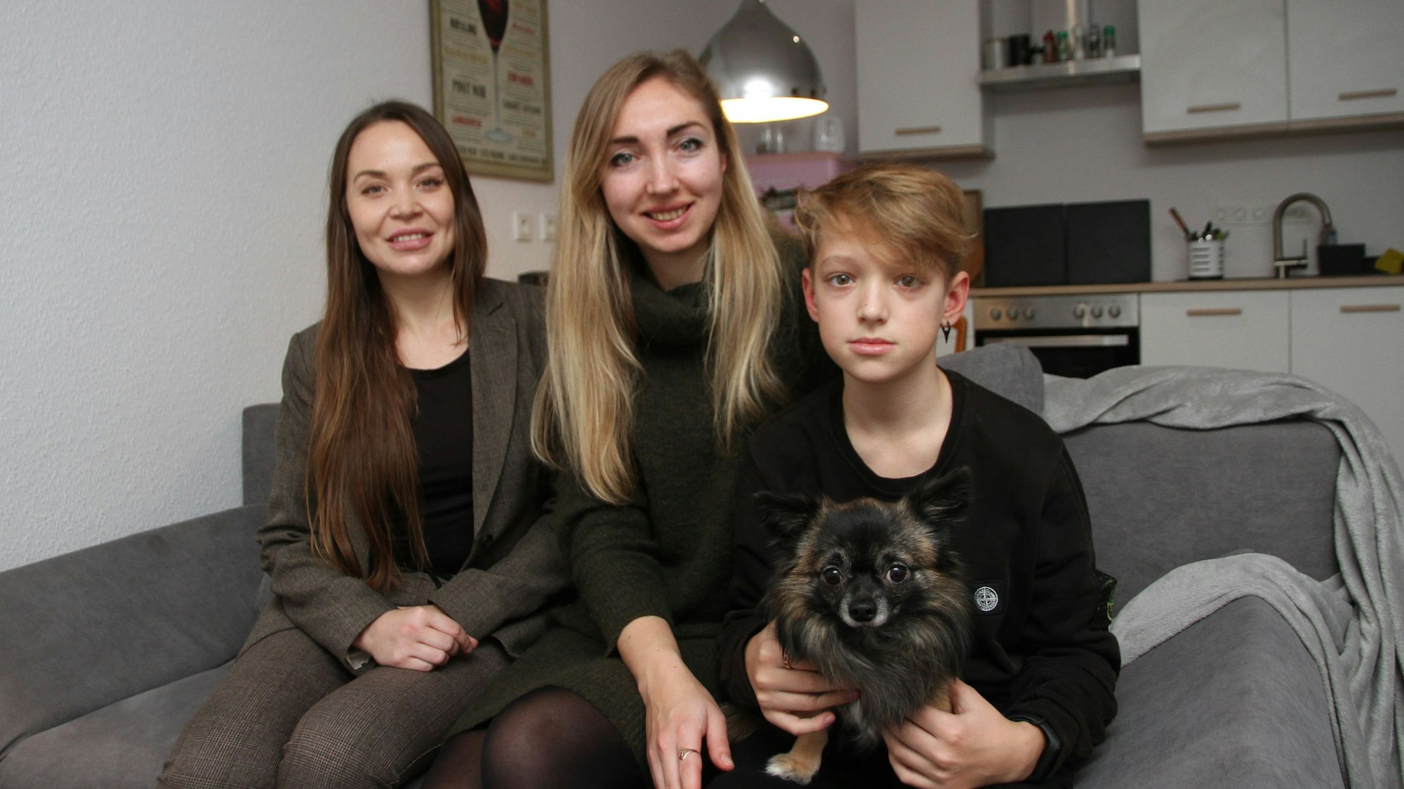 Die drei sitzen mit dem Chihuahua auf einem Sofa in ihrer Küche.