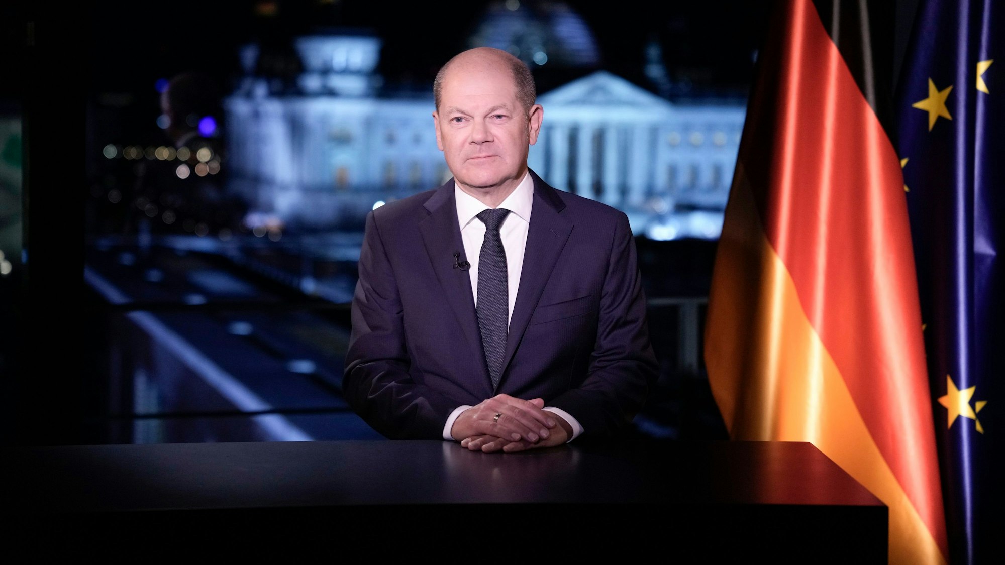 Bundeskanzler Olaf Scholz sitzt an einem Tisch, neben ihm sind die Fahnen der Bundesrepublik Deutschland und der Europäischen Union.