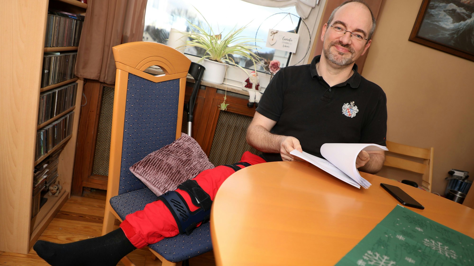 Alexander Pfister sitzt kurz nach der Entlassung 2022 im Wohnzimmer seiner Wohnung, sein Bein ist geschient.