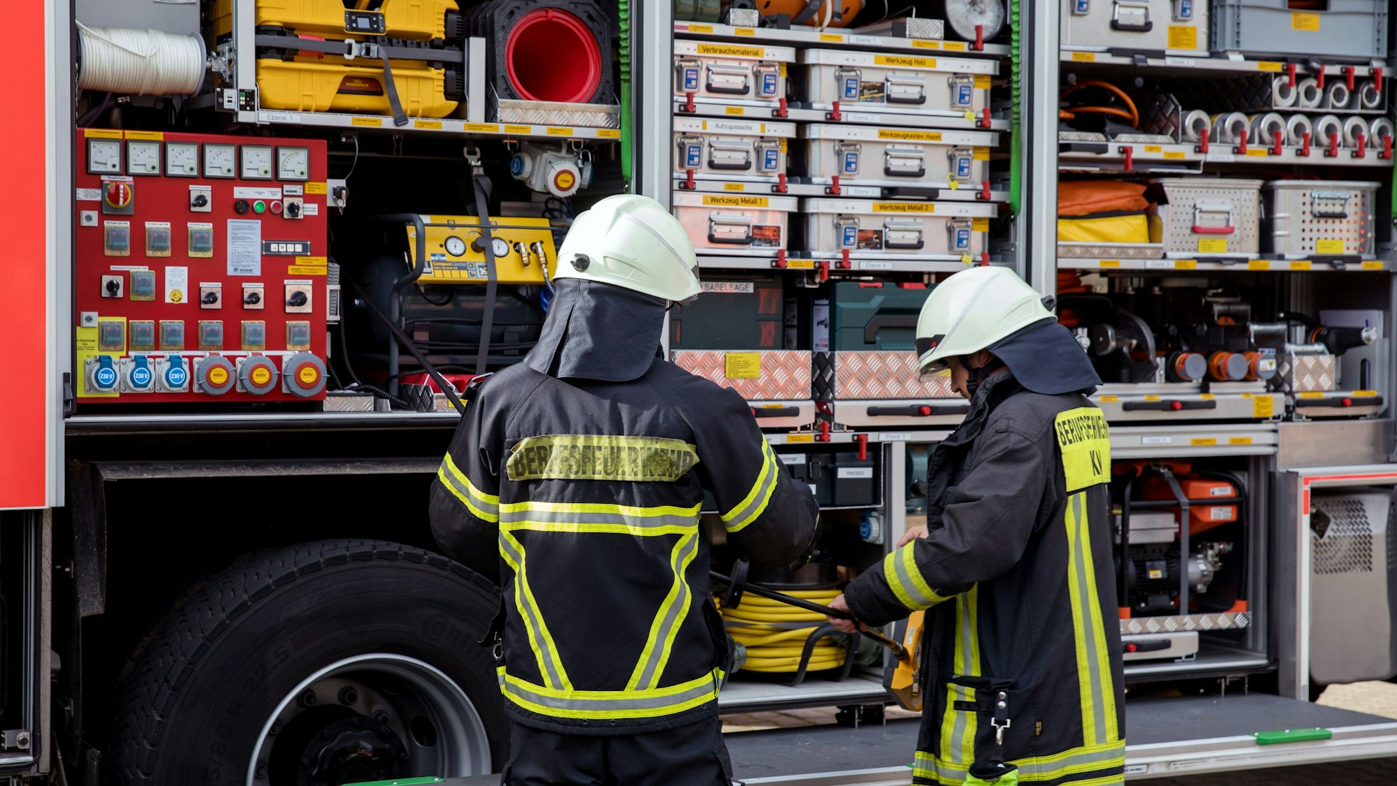Einsatzkräfte der Feuerwehr stehen an einem Feuerwehrfahrzeug.