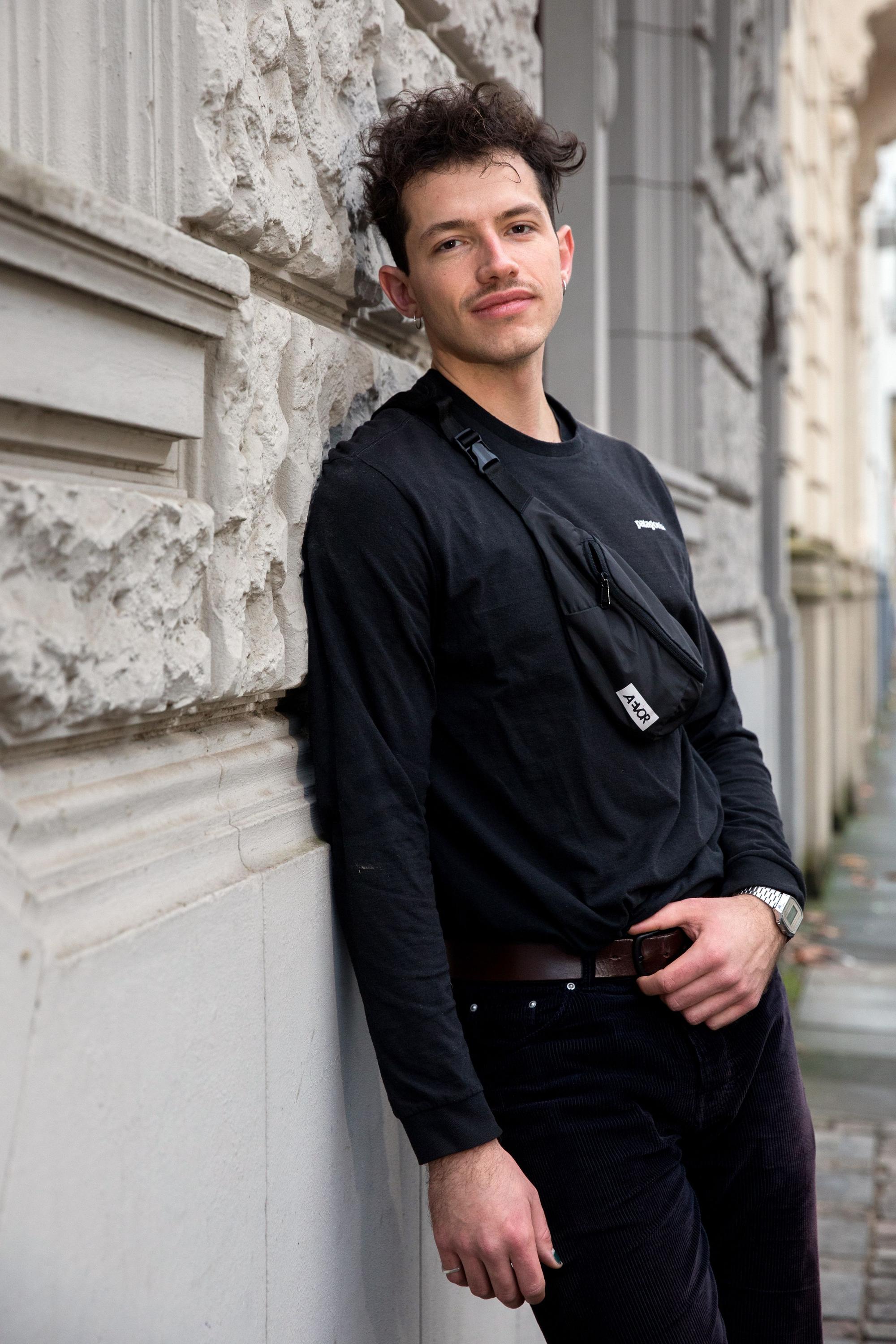 Paul Köninger steht seitlich an einer sandfarbenen Wand angelegt. Er ist komplett in schwarzs gekleidet.