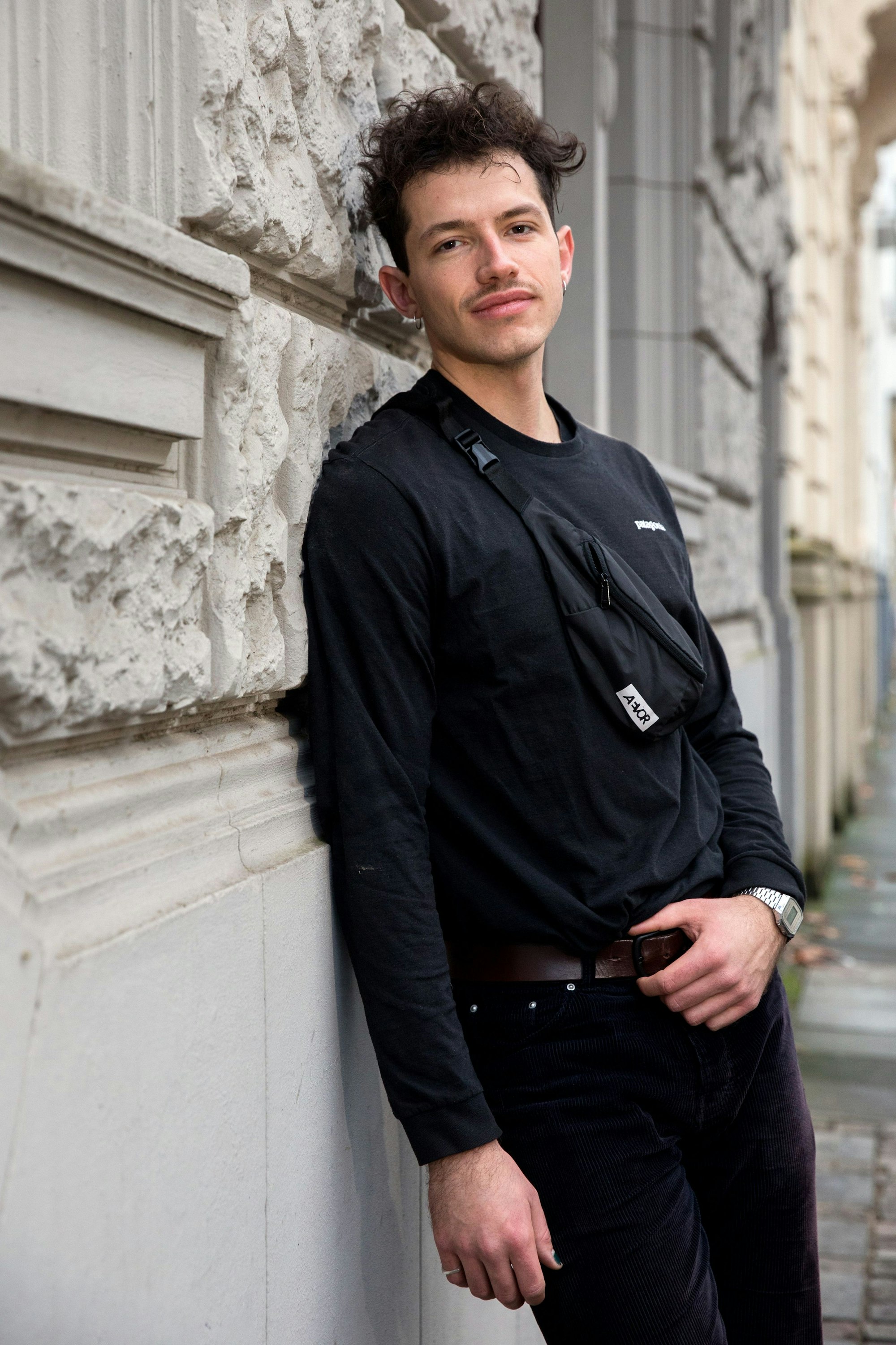 Paul Köninger steht seitlich an einer sandfarbenen Wand angelegt. Er ist komplett in schwarzs gekleidet.