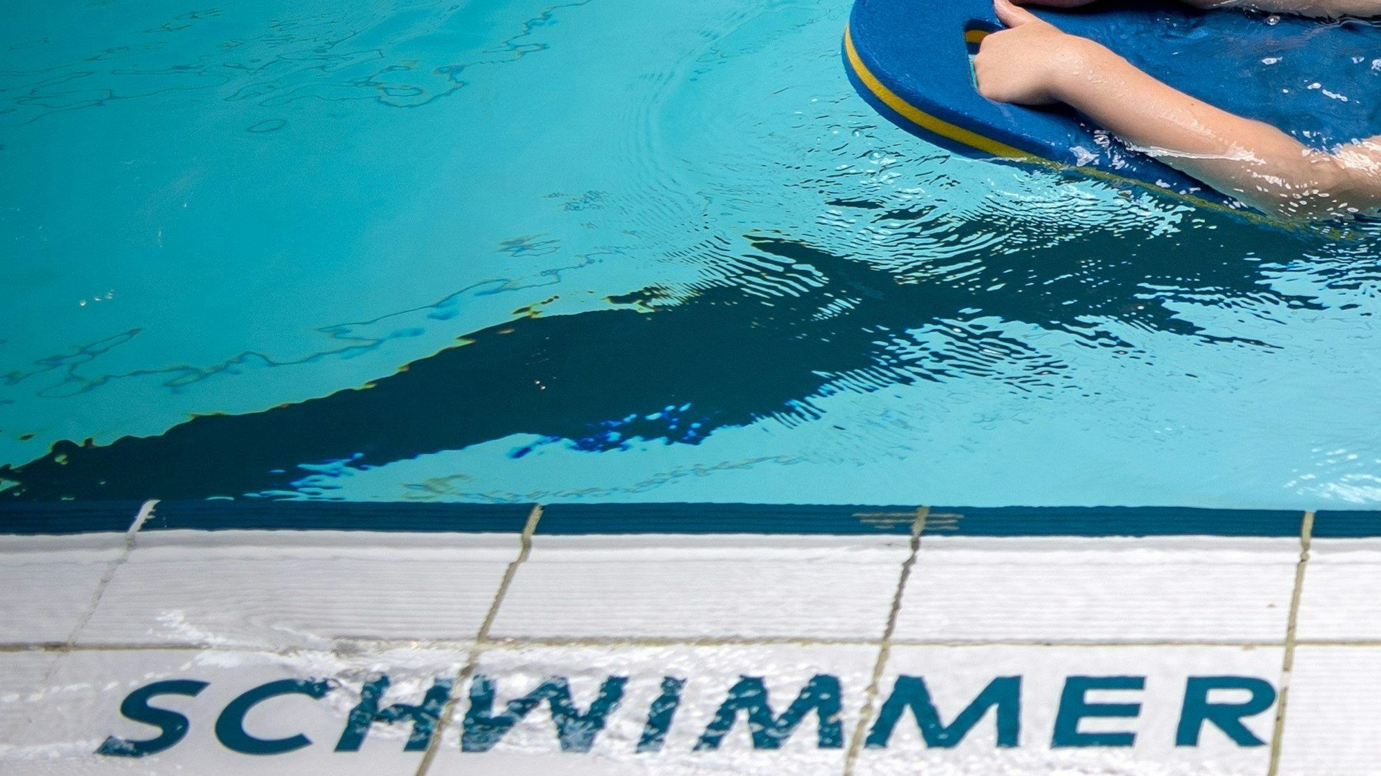 Ein Kind schwimmt mit Brett in einem Schwimmbecken.