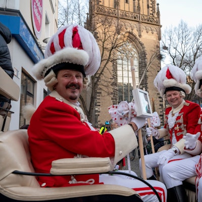 Das Dreigestirn sitzt in einer Kutsche und lächelt in die Kamera.