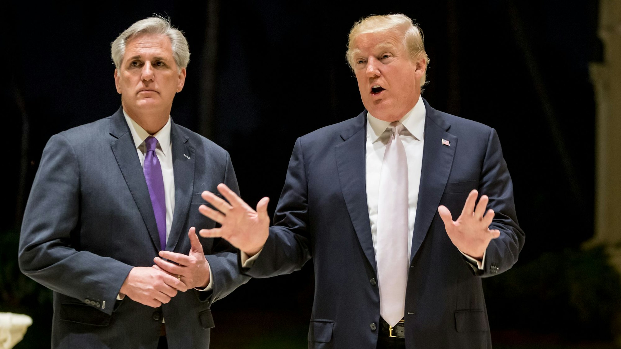 Die Politiker Kevin McCarthy und Donald Trump beantworten im Anzug Fragen von Journalisten, Trump hebt beschwichtigend die Hände.