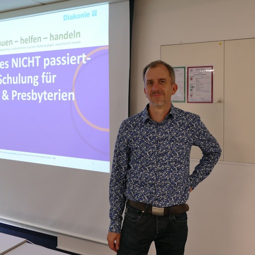 Christian Gröger steht vor einer Leinwand, an die projiziert steht: „Damit es NICHT passiert – Schulung für KSV & Presbyterien“.
