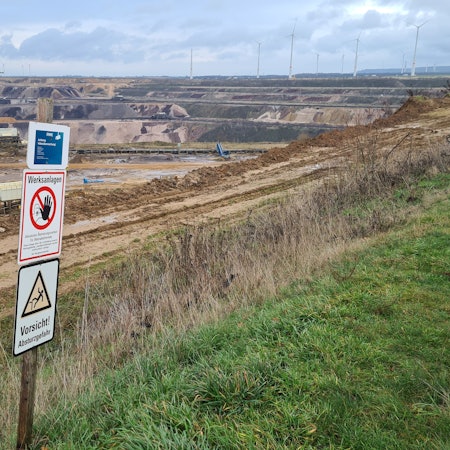 Der Tagebau Garzweiler. Im Vordergrund stehen Schilder, die zur Vorsicht mahnen.