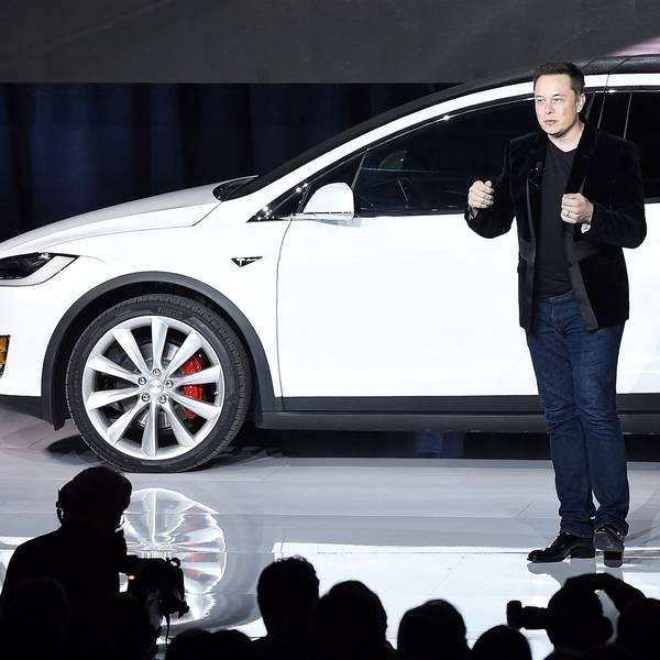 Elon Musk spricht auf einer Bühne im September 2015 zur Einführung des Tesla X. Im Hintergrund ist ein weißes Exemplar des Autos zu sehen.