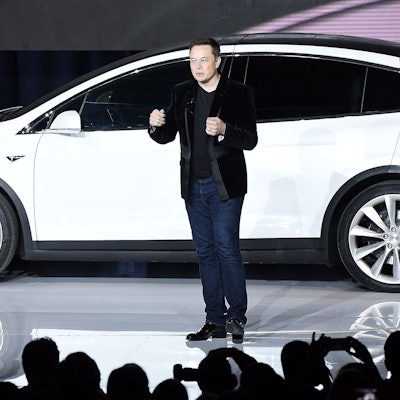 Elon Musk spricht auf einer Bühne im September 2015 zur Einführung des Tesla X. Im Hintergrund ist ein weißes Exemplar des Autos zu sehen.