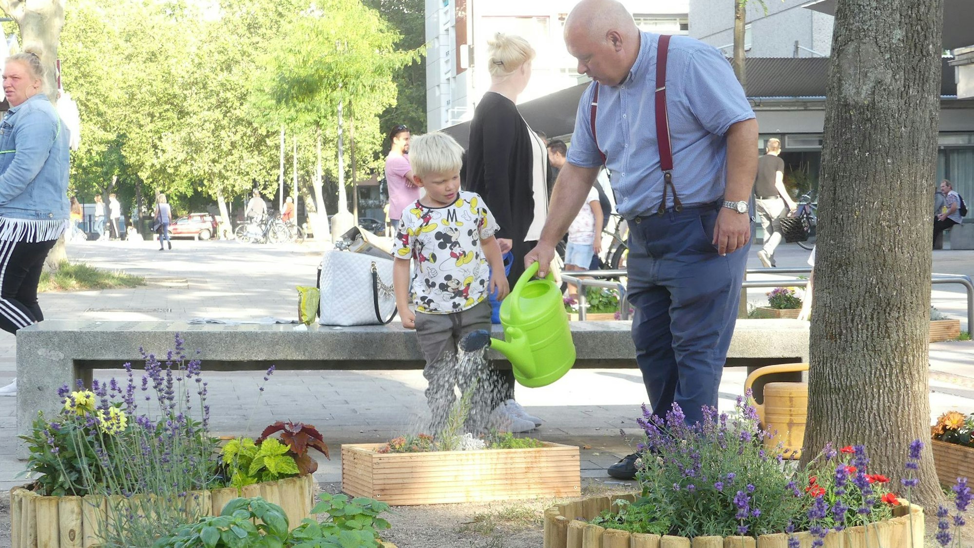 Streetworker Antonio Pizzulli steht mit einem kleinen Jungen in der Bocklemünder Fußgängerzone und gießt dort selbst angelegte Blumenbeete.