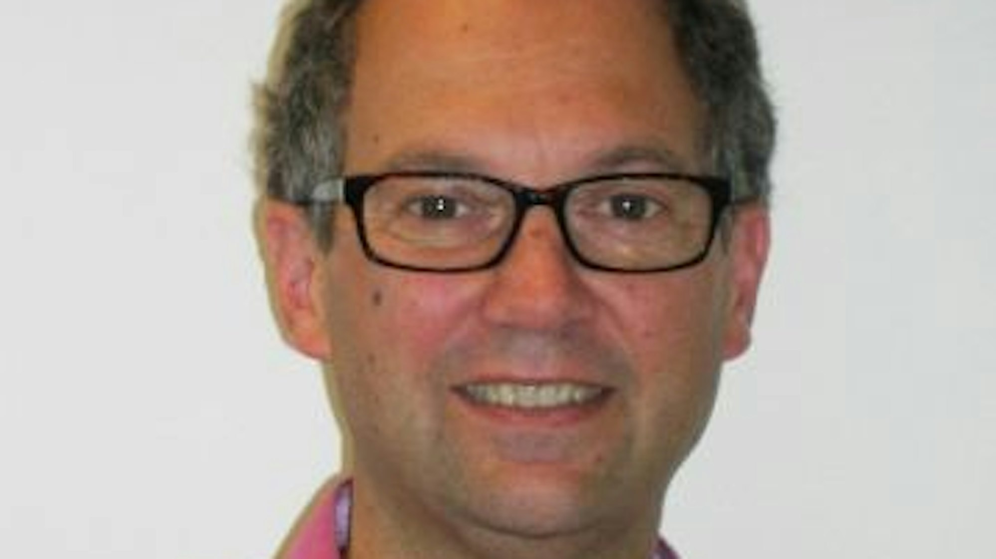 Achim Stahl guckt für ein Porträtfoto in die Kamera. Er trägt eine schwarze Hornbrille und ein pinkfarbenes Hemd.