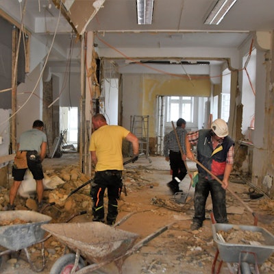 Vier Männer schaufeln den Schutt aus einem zerstörten Haus in Schubkarren.