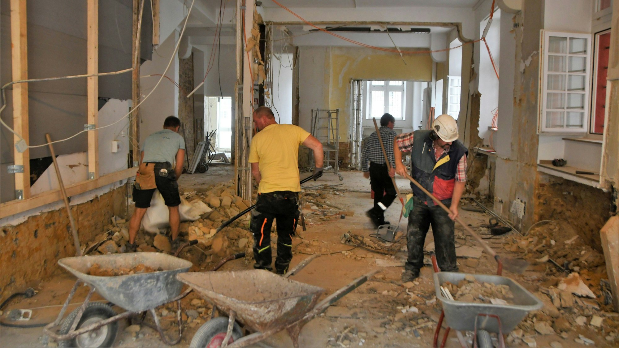 Vier Männer schaufeln den Schutt aus einem zerstörten Haus in Schubkarren.