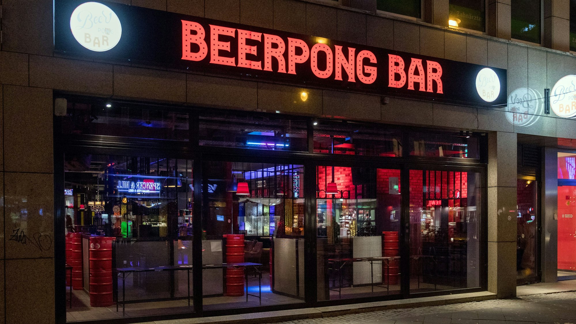 Die Beerpongbar von außem bei Dunkelheit. Der rote Schriftzug ist beleuchtet.