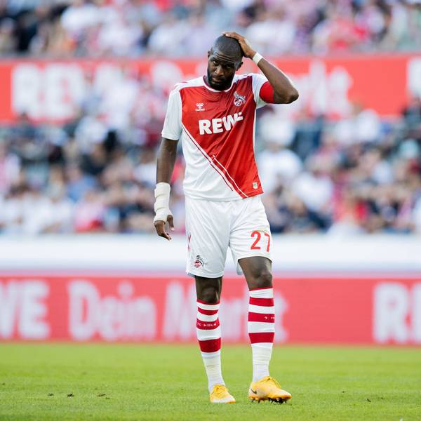 Der Fußballprofi Anthony Modeste steht im FC-Trikot auf dem Platz und greift sich an den Kopf.
