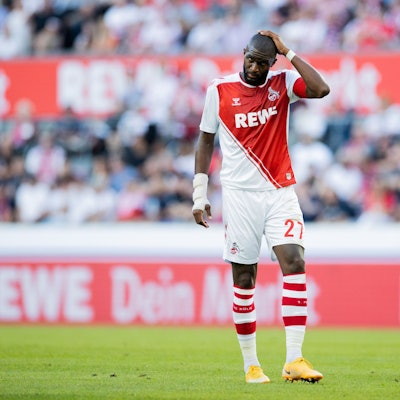 Der Fußballprofi Anthony Modeste steht im FC-Trikot auf dem Platz und greift sich an den Kopf.