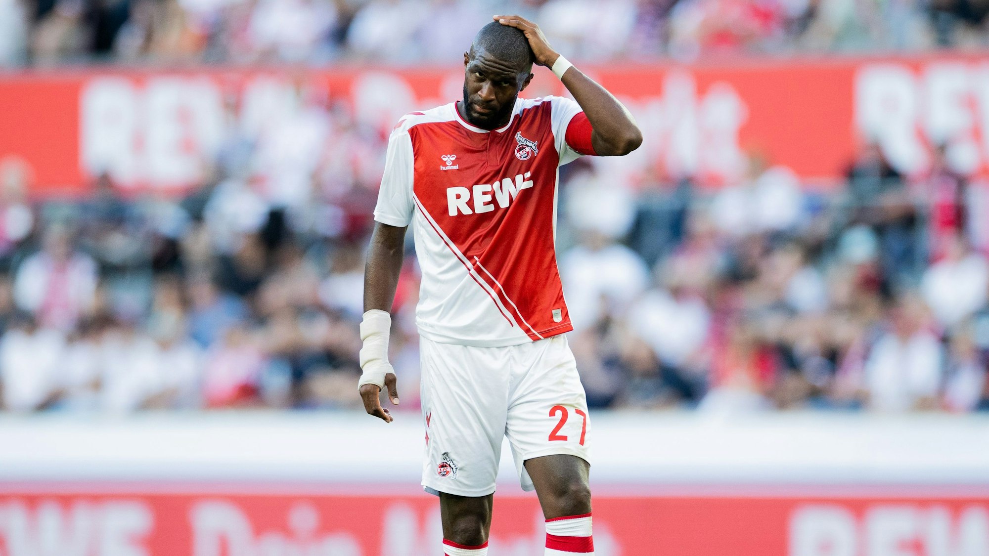Der Fußballprofi Anthony Modeste steht im FC-Trikot auf dem Platz und greift sich an den Kopf.