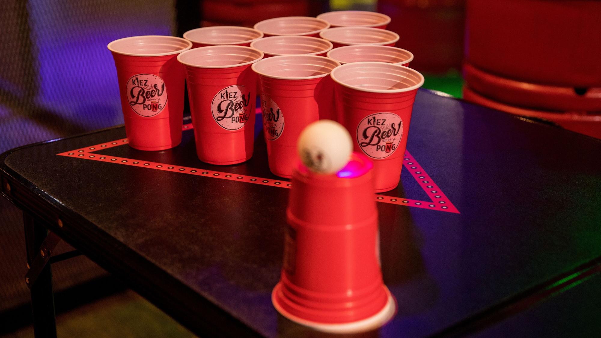 Rote Plastikbecher stehen in einem Dreieck auf einem Tisch. Der Aufbau eignet sich zum Beerpongspielen.