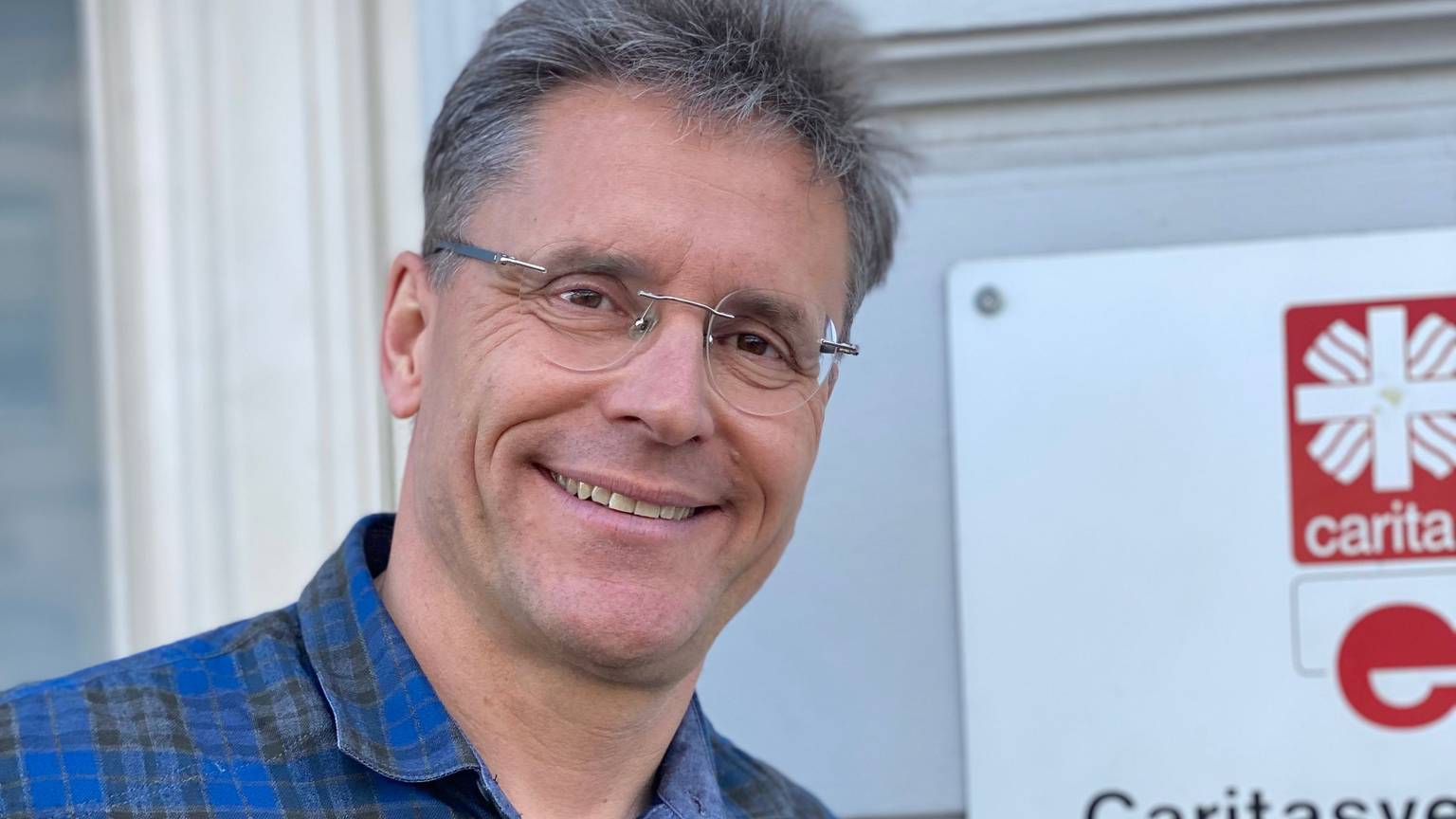 Ralf Klaes steht vor einer Wand, an der ein Schild der Caritas zu erkennen ist.