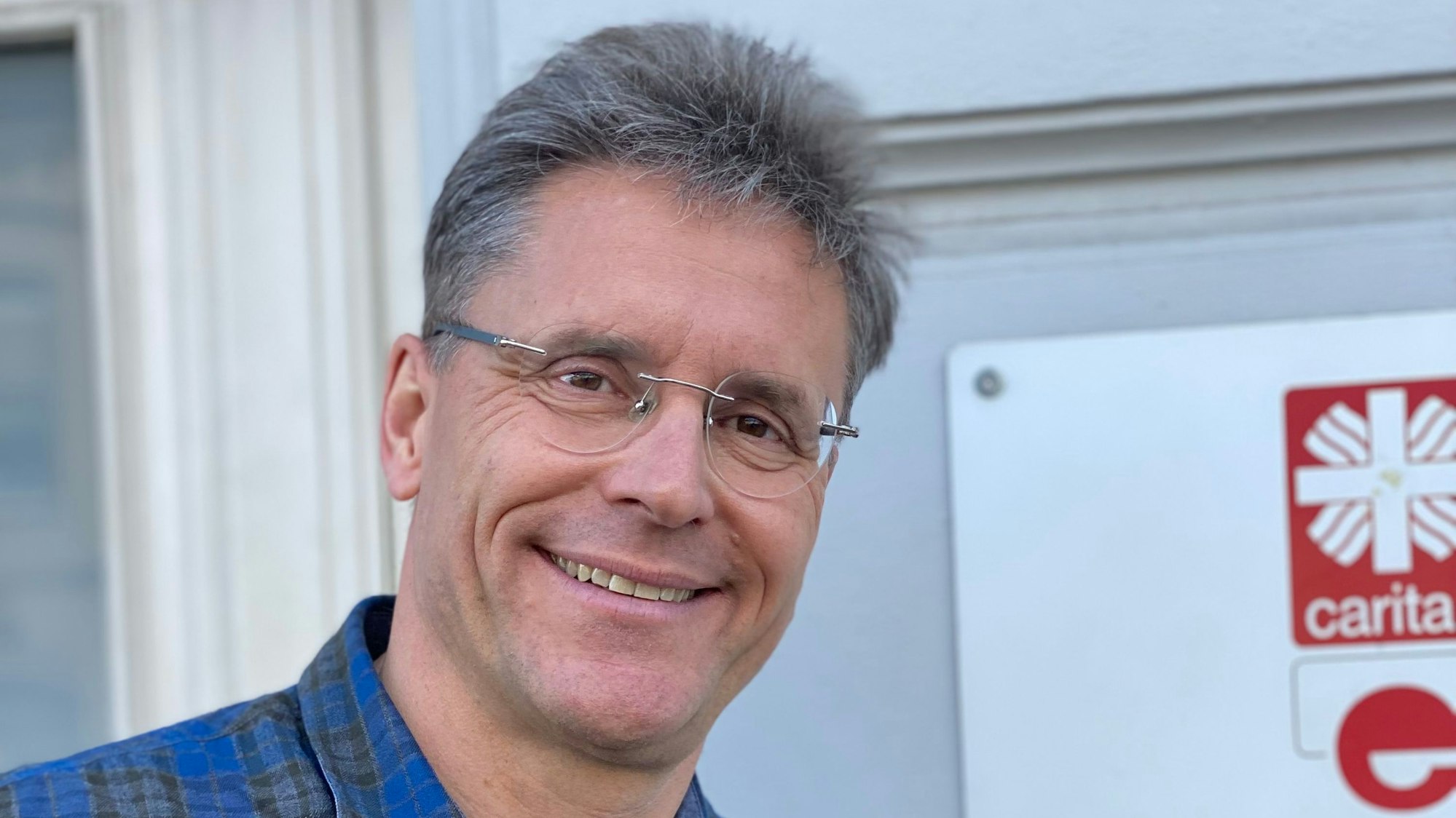 Ralf Klaes steht vor einer Wand, an der ein Schild der Caritas zu erkennen ist.