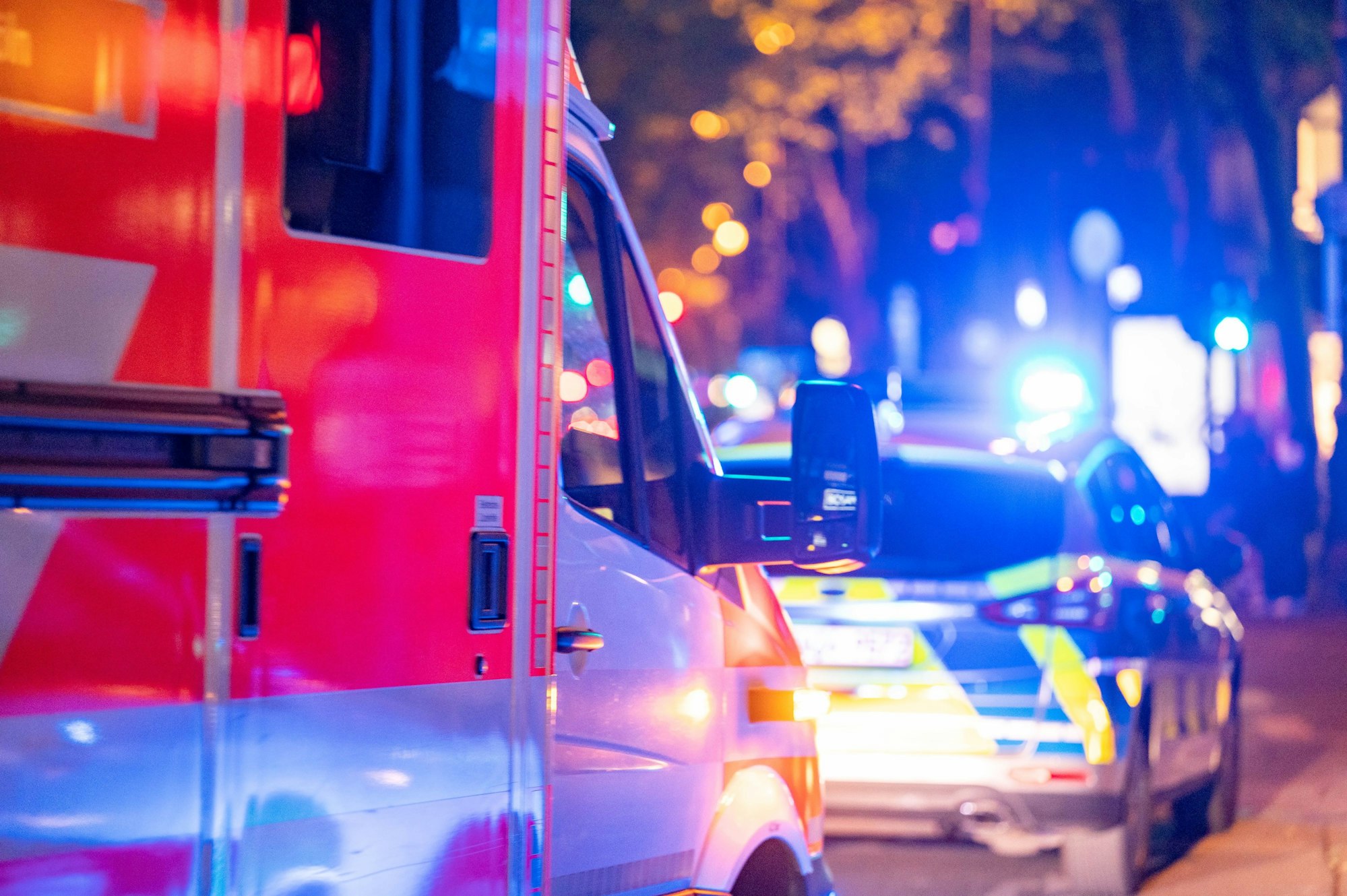 Polizei und ein Rettungswagen fahren nachts über eine Straße.