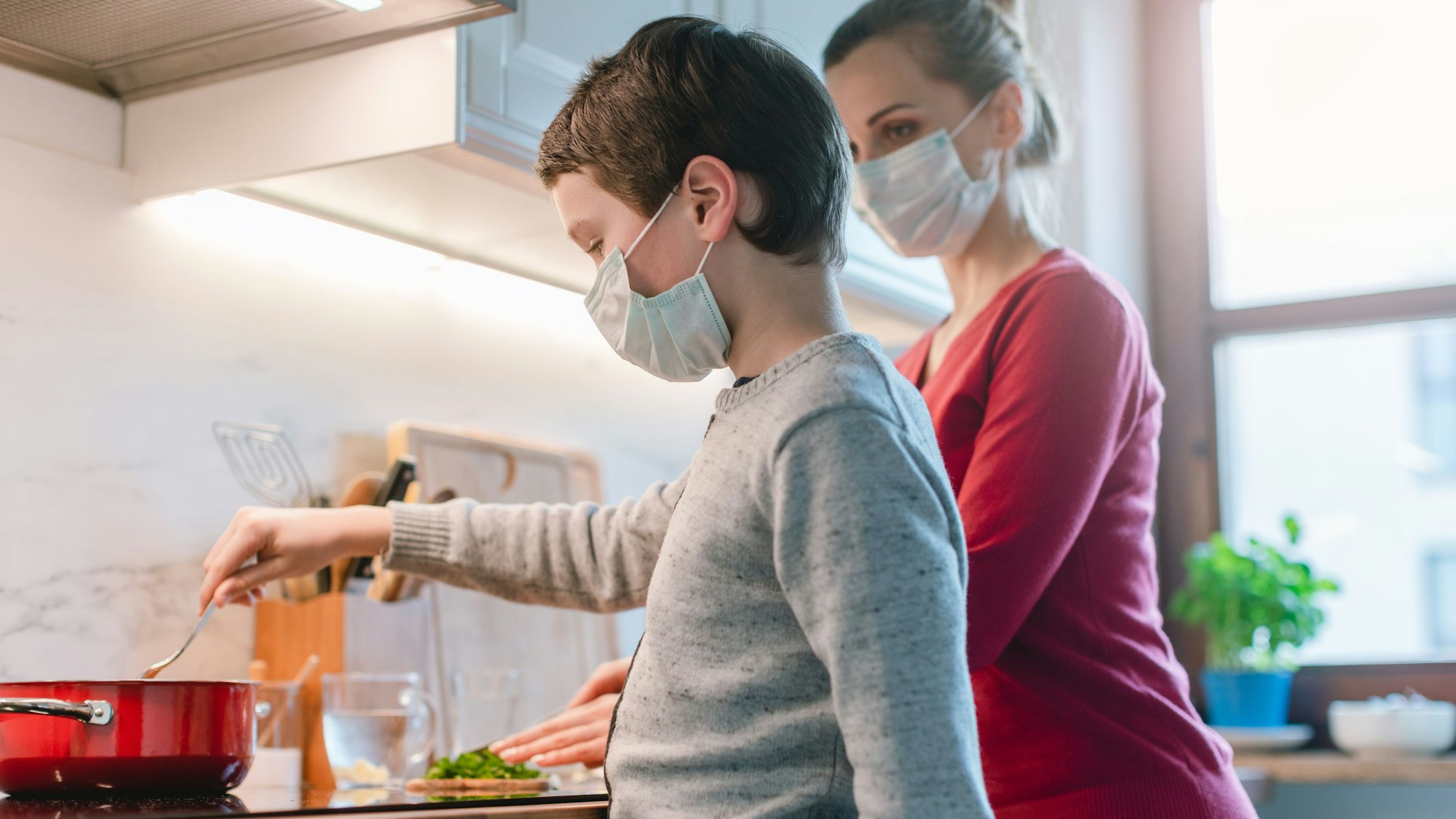 Mutter und Sohn kochen zusammen in der Küche, beide tragen eine Maske.