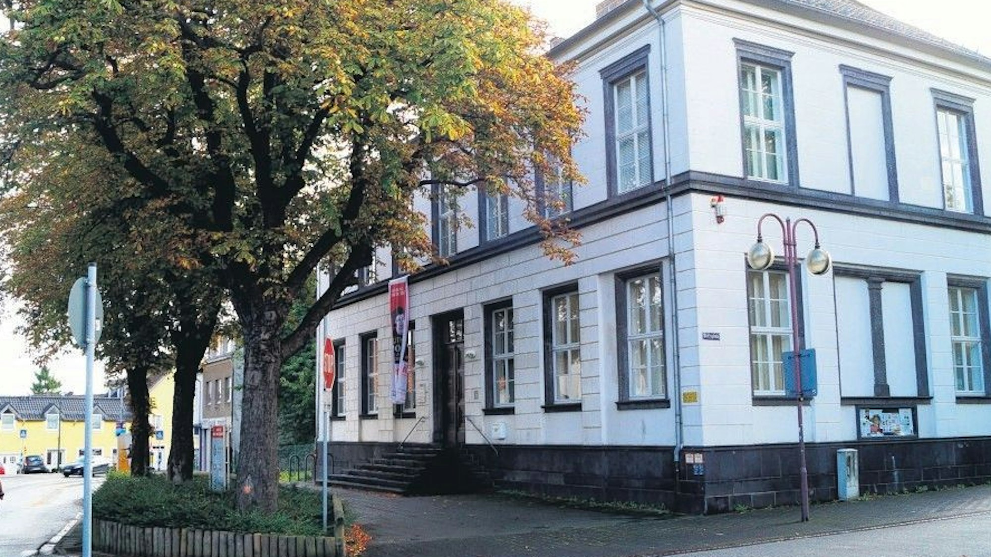 Das Haus für Kunst und Geschichte, ein weißes Gebäude an einer Straßenecke. Davor steht ein herbstlich belaubter Baum und einige Schilder.