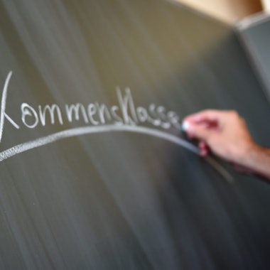 Eine Hand schreibt mit weißer Kreide das Wort „Willkommensklasse“ an eine Tafel.