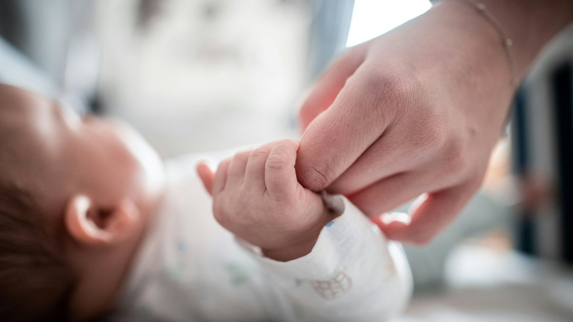 Ein Baby klammert sich an den Finger seiner Mutter.