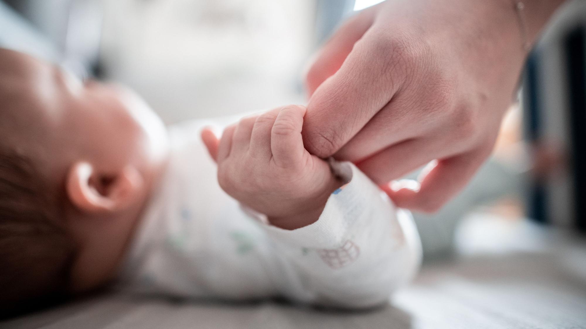 Ein Baby klammert sich an den Finger seiner Mutter.