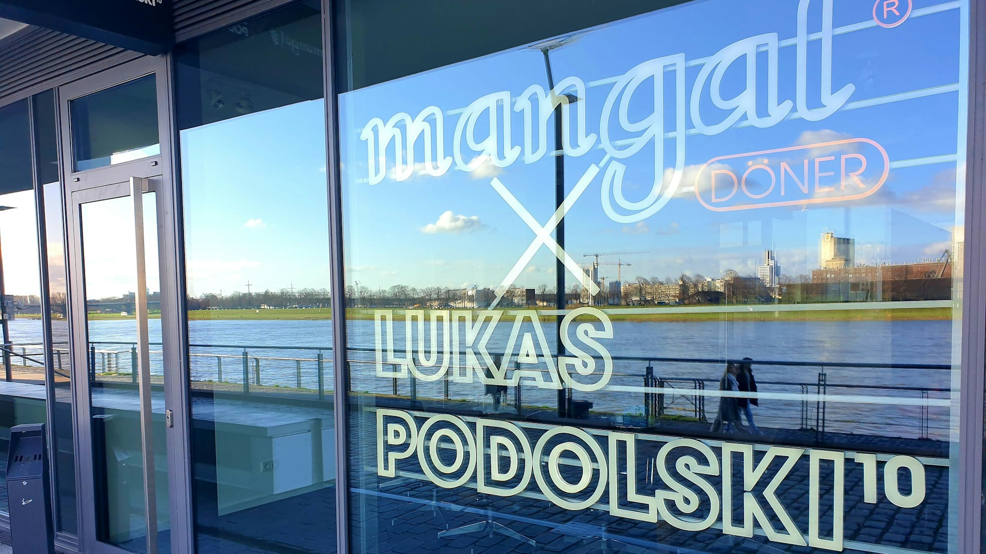 Im Fenster des Büros hängt das große Logo der Firma, in den Scheiben spiegelt sich der Rhein.