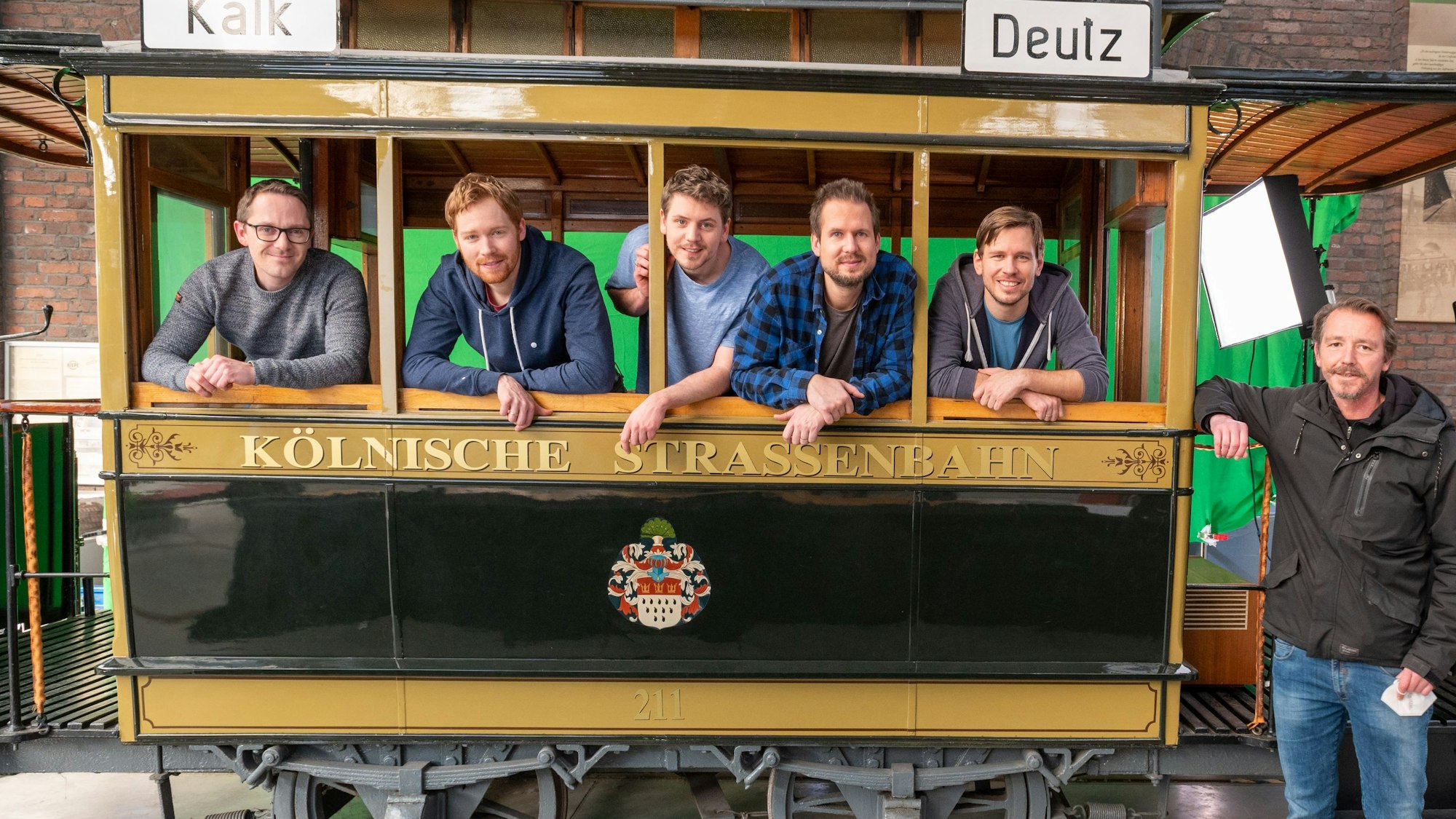 Die Band Miljö und der Filmemacher Herbert Rheindorf stehen in einer historischen Strassenbahn im Straßenbahnmuseum Thielenbruch.