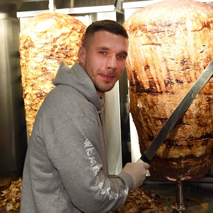 Lukas Podolski steht bei der Eröffnung eines Döner-Ladens an einem Dönerspieß.