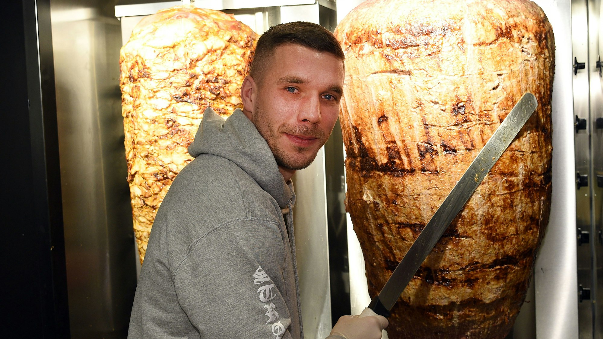 Fußball-Weltmeister Lukas Podolski steht bei der Eröffnung eines Dönerladens an einem Dönerspieß. (Symbolbild)