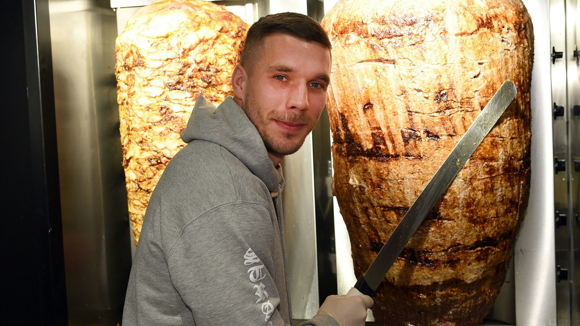 Lukas Podolski steht an einem Dönerspieß.
