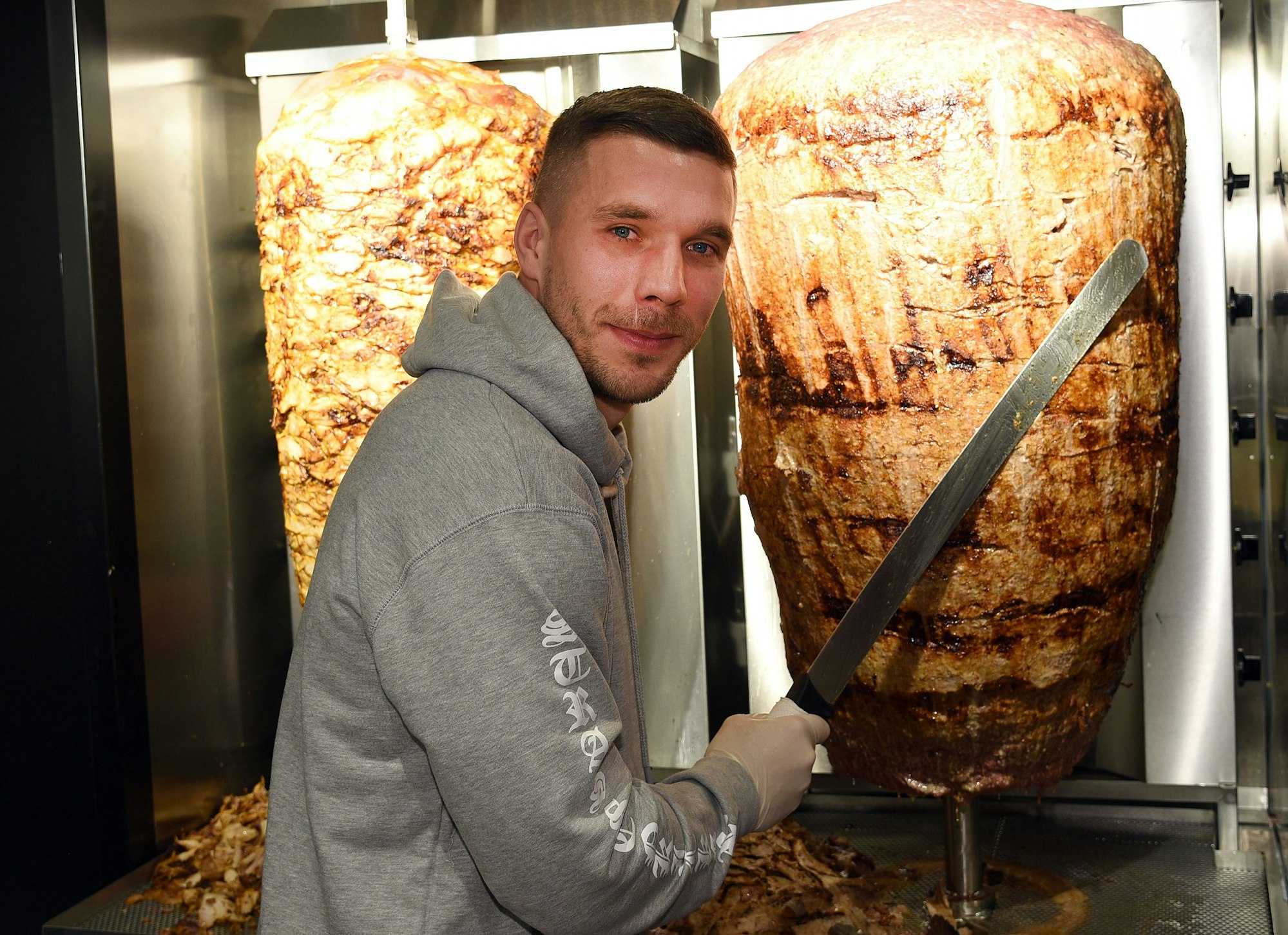 Lukas Podolski steht mit einem Messer am Dönerspieß.