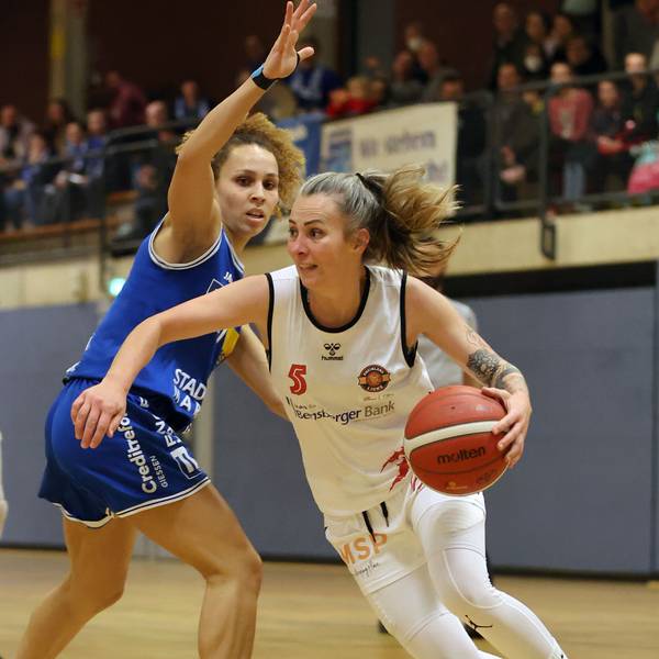 Im weißen Trikot führt die Spielerin der Rheinland Lions den Ball an der Hand. Ihre Gegnerin im blauen Trikot versucht sie daran zu hindern.