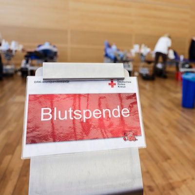 Ein Schild mit der Aufschrift „Blutspende“. Im Hintergrund sind mehrere Liegen aufgebaut.