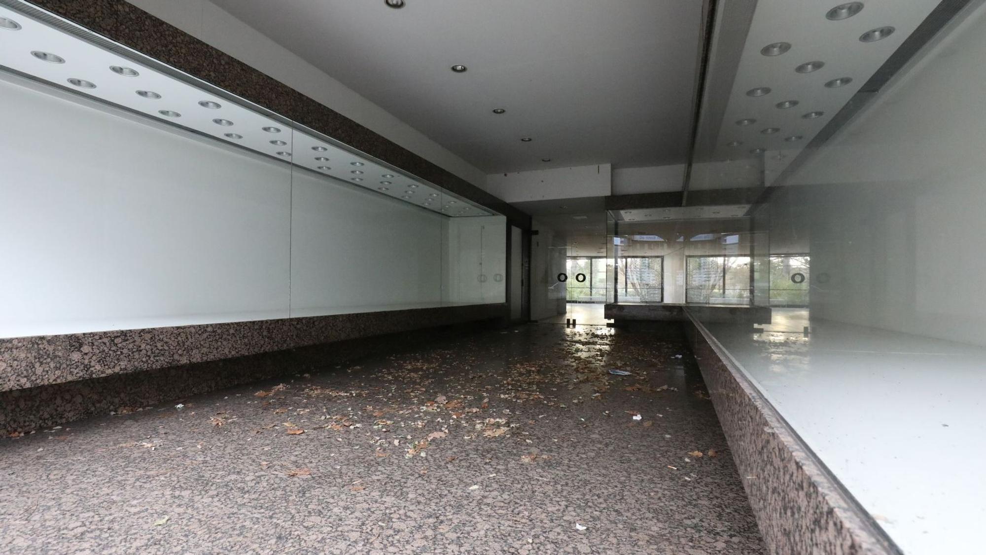 Vor den Eingang eines Geschäftes an der Hauptstraße, dessen Auslagen hinter den Fensterfronten leer sind, hat der Wind Laub geweht.