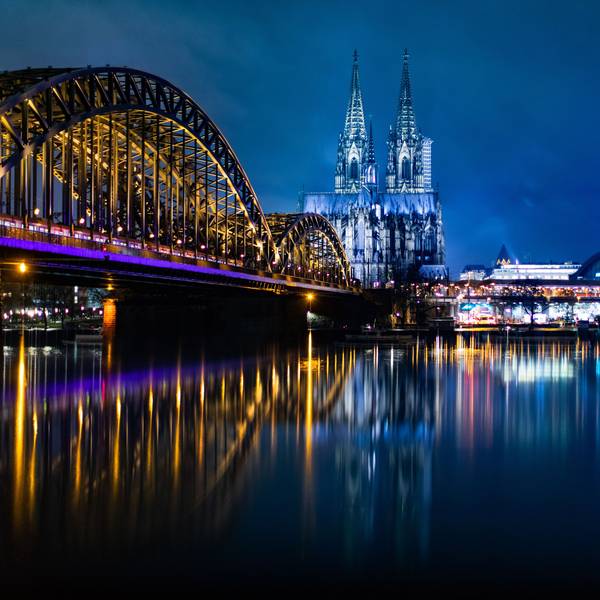 Die bunt beleuchtete Hohenzollernbrücke mit dem Kölner Dom und dem Musical Dome bei Nacht.