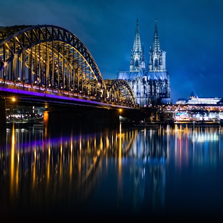 Die bunt beleuchtete Hohenzollernbrücke mit dem Kölner Dom und dem Musical Dome bei Nacht.