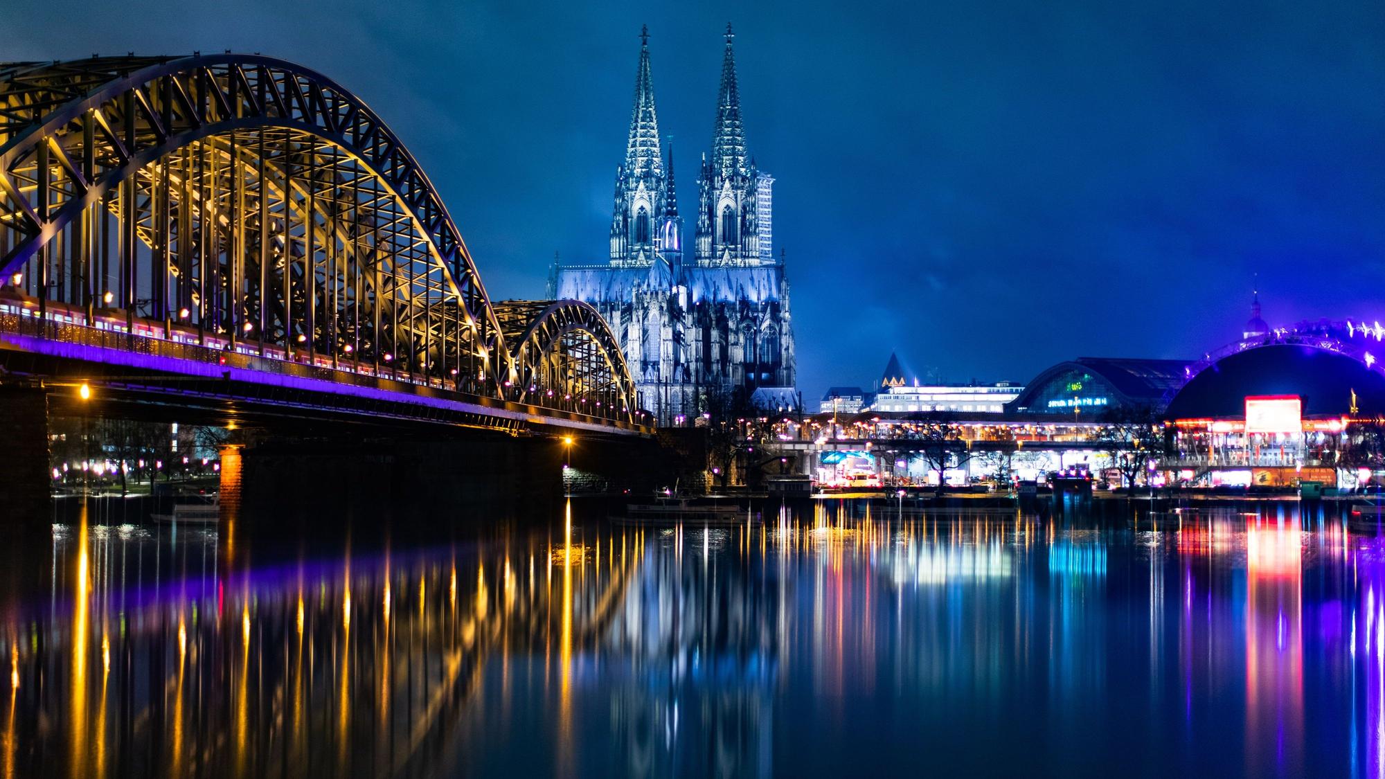 Die bunt beleuchtete Hohenzollernbrücke mit dem Kölner Dom und dem Musical Dome bei Nacht.