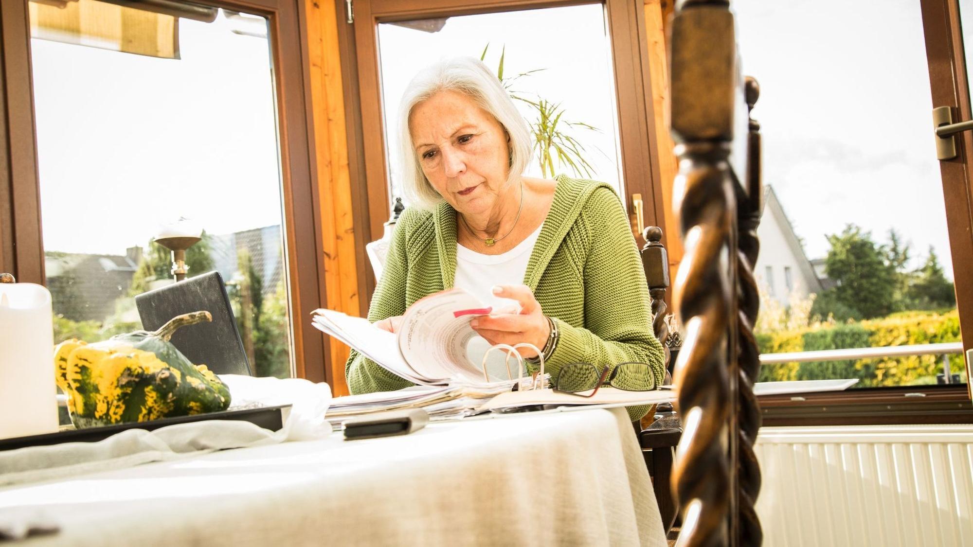 Eine ältere Frau sitzt an einem Tisch und blättert in einem Aktenordner.