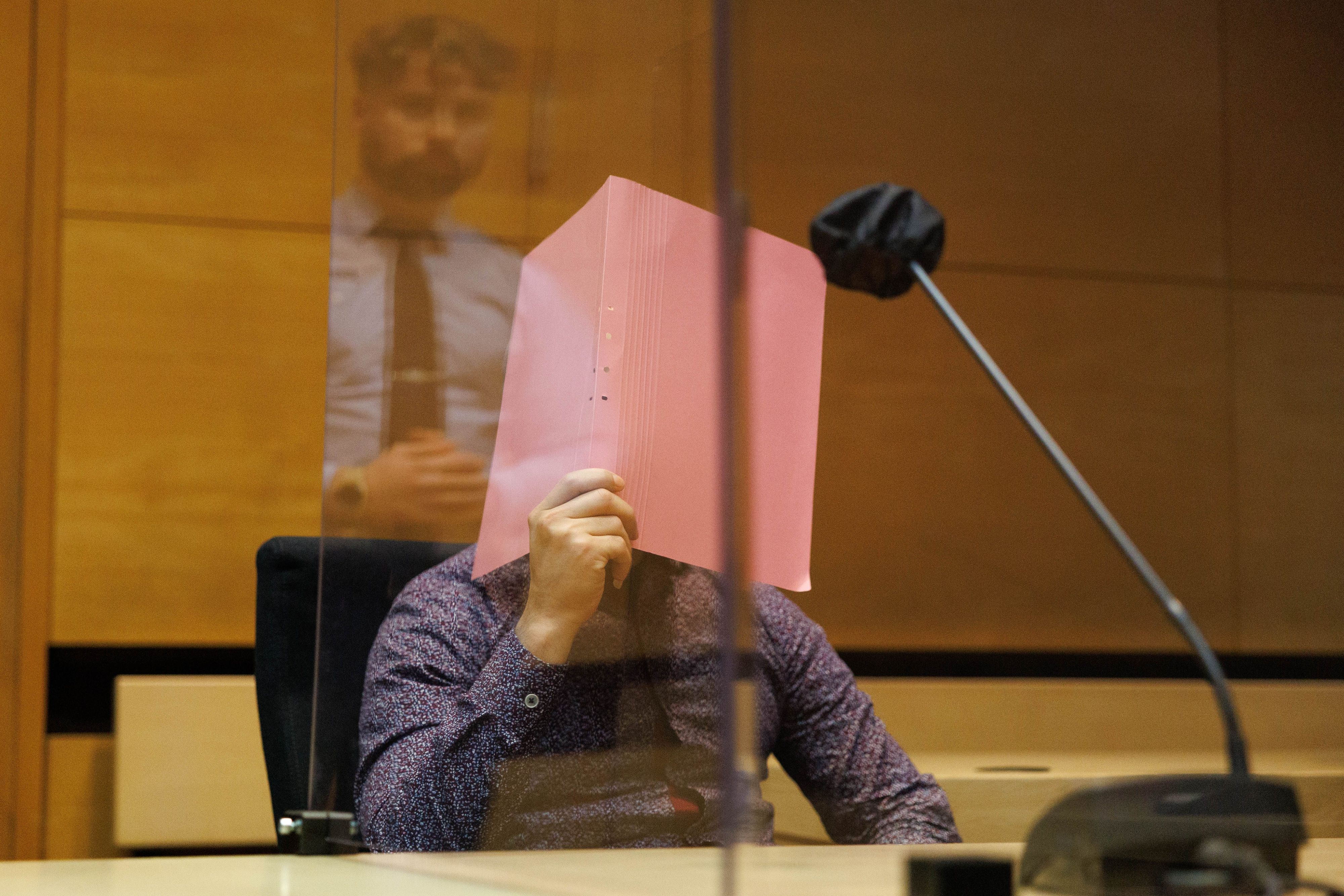 04.01.2023, Nordrhein-Westfalen, Bielefeld: Der Angeklagte sitzt in einem Saal vom Landgericht zum Auftakt im Prozess um einen Streit wegen zu lauter Musik, in der Scheibe spiegelt sich ein Justizbeamter.