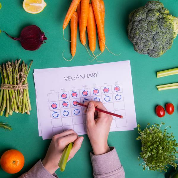 Jemand füllt einen Veganuary-Plan aus, darum liegt verschiedenen Obst und Gemüse.