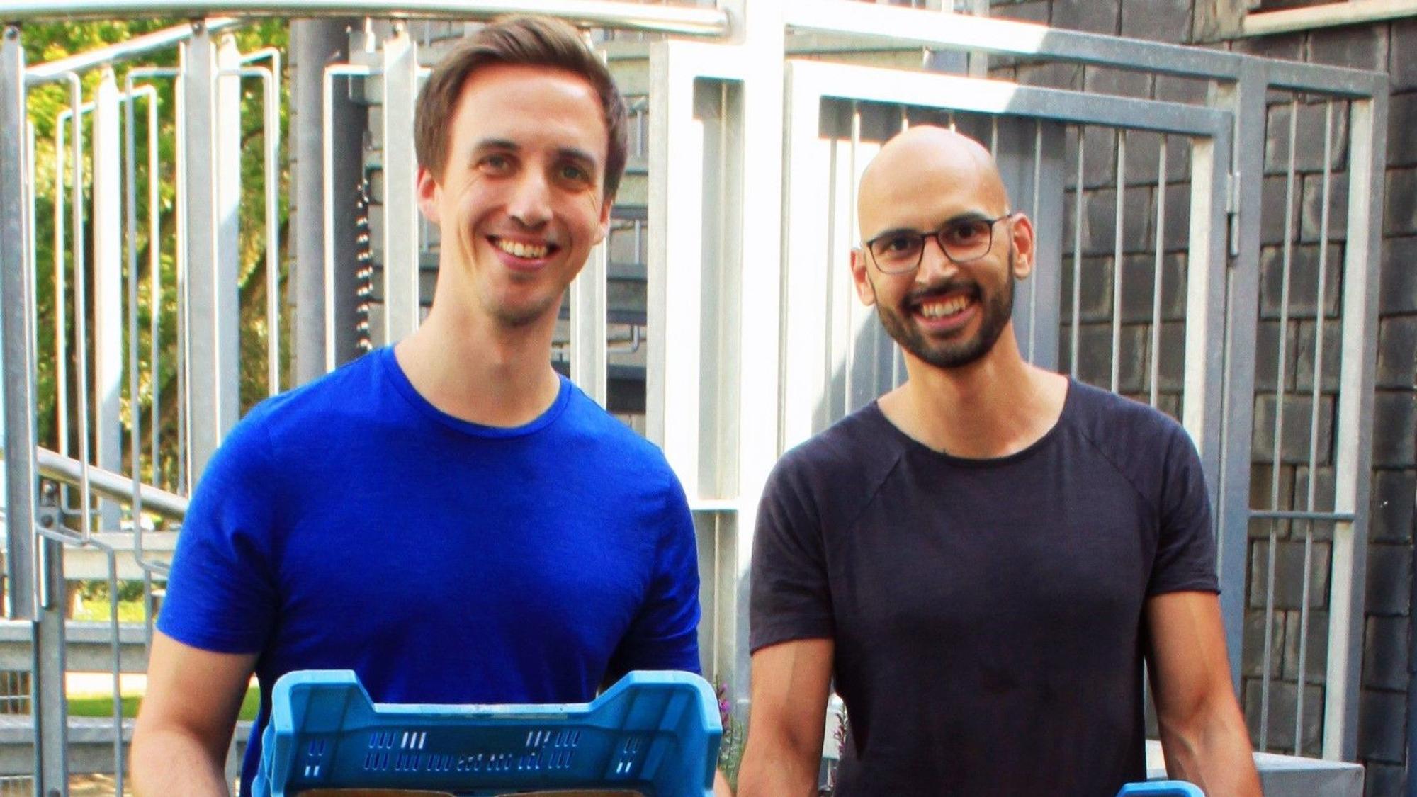 Johannes Decker und Daniel Neumann halten Gemüsekisten in den Händen und lächeln in die Kamera.