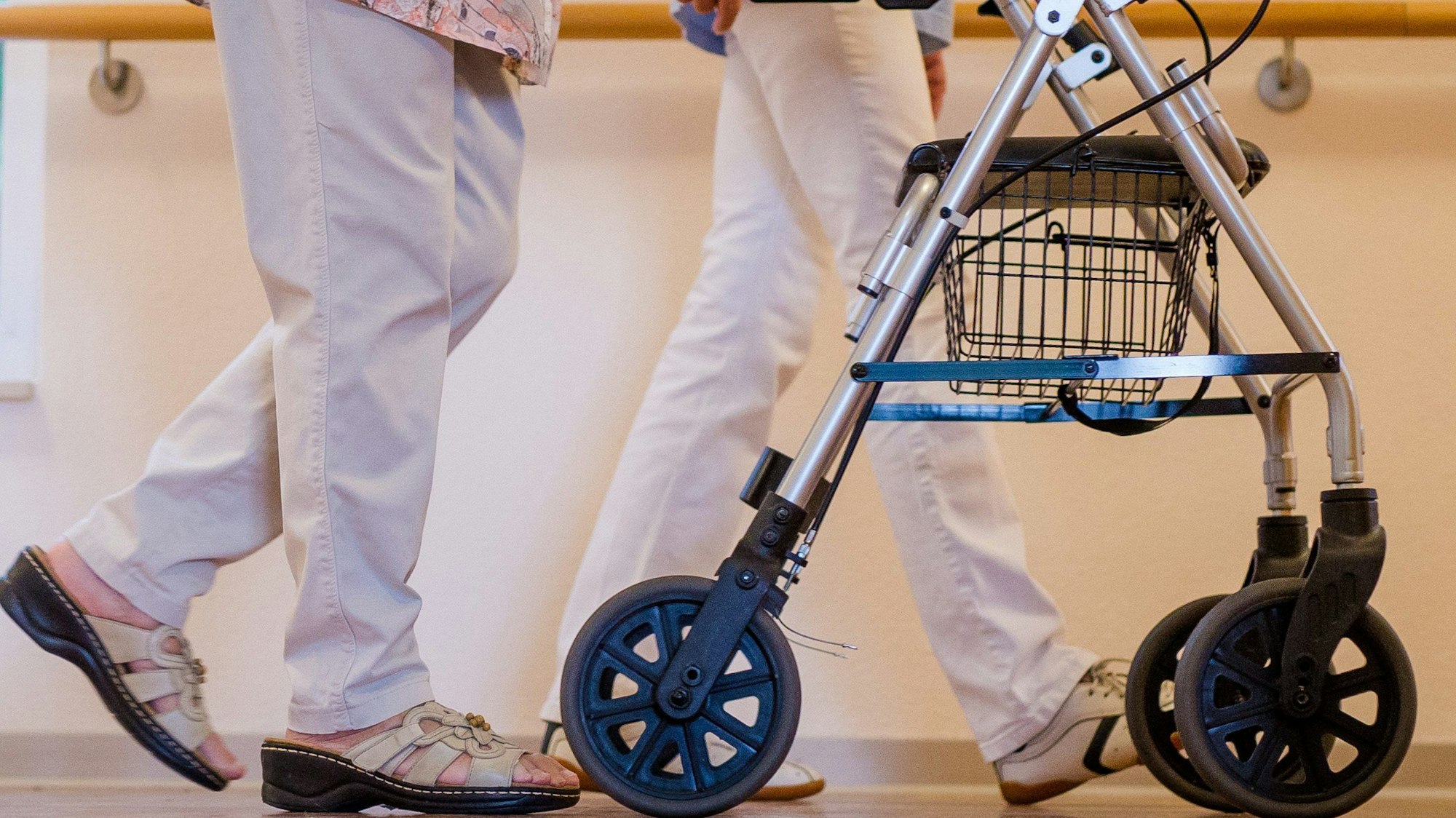 Eine Pflegekraft geht in einem Pflegeheim mit einer älteren Frau über einen Korridor.