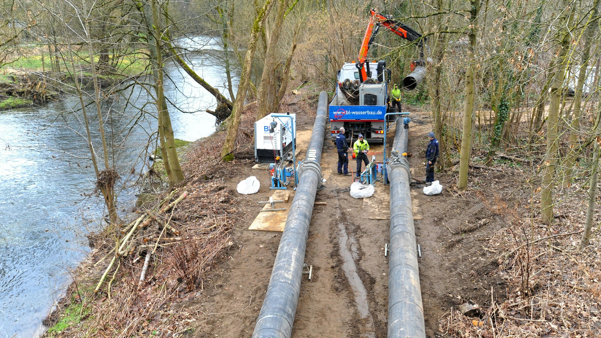 Arbeiter verbinden dicke schwarze Rohre mithilfe eines Baggers im Wald nebend er Wupper.